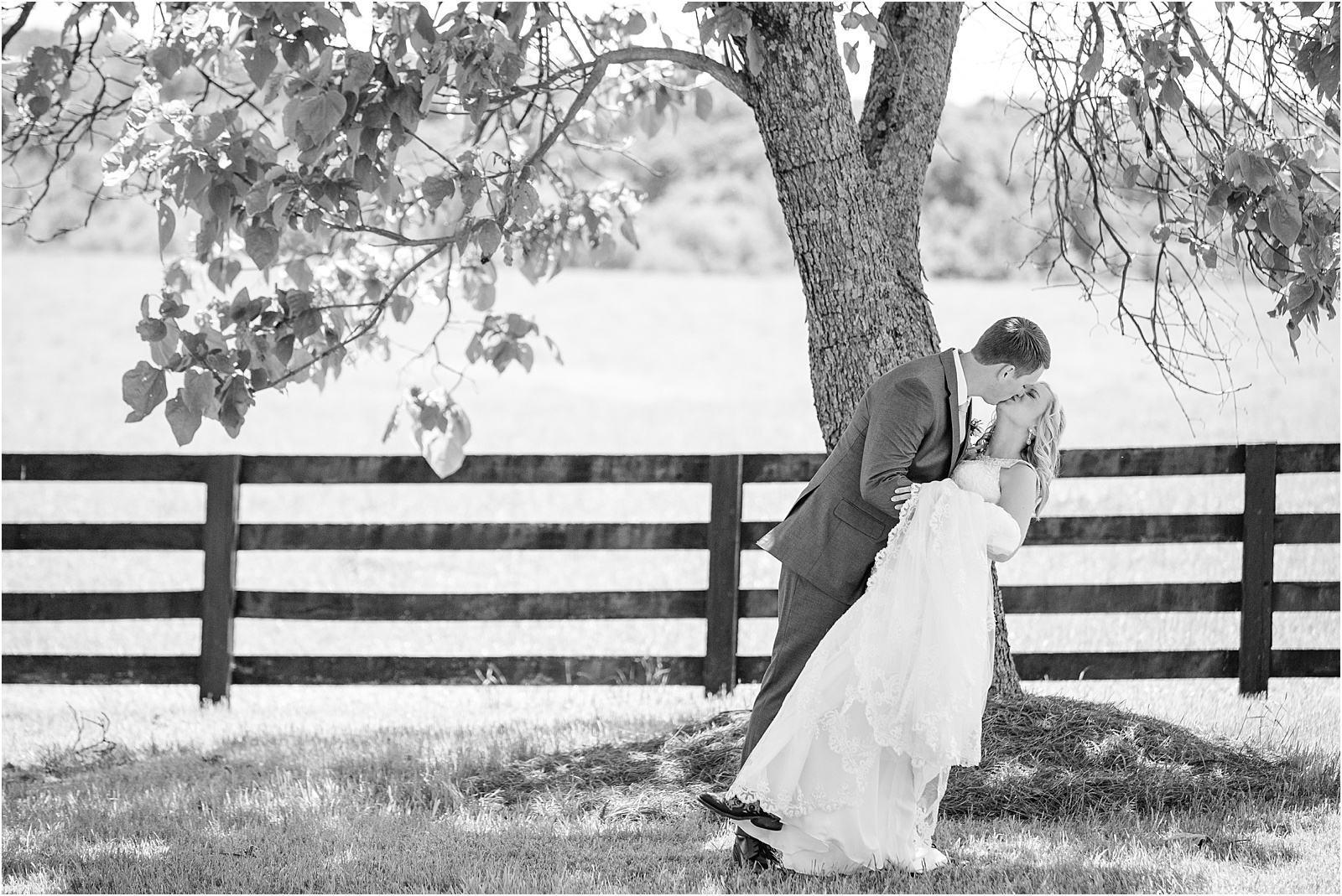 Groom dips bride in a field next to a wooden fence