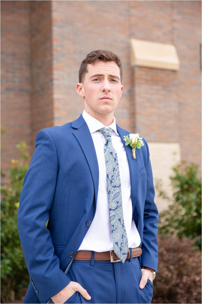 Groom in blue suit posing for wedding photographer before ceremony
