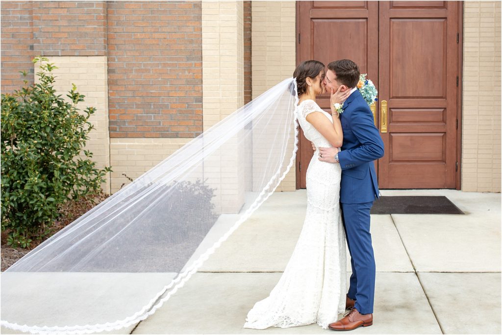 Bride and groom kiss with veil flowing in the wind