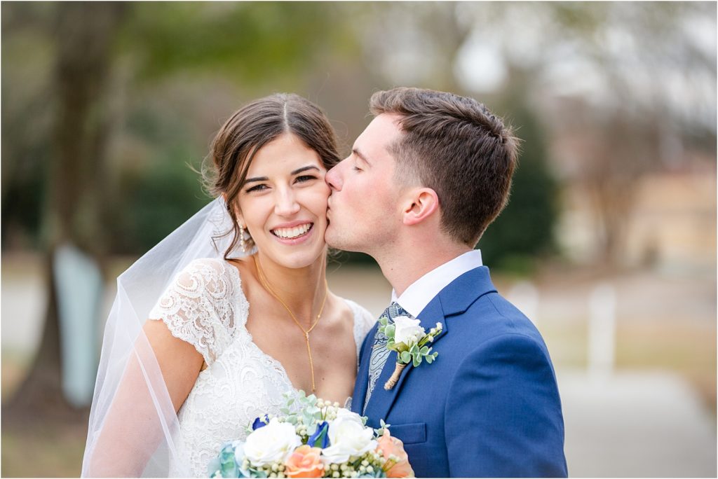 groom in blue suit kissing bride's cheek