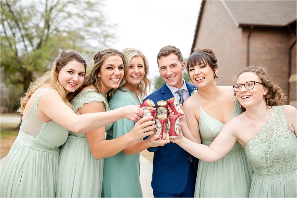 Groom holds beer with bridesmaids