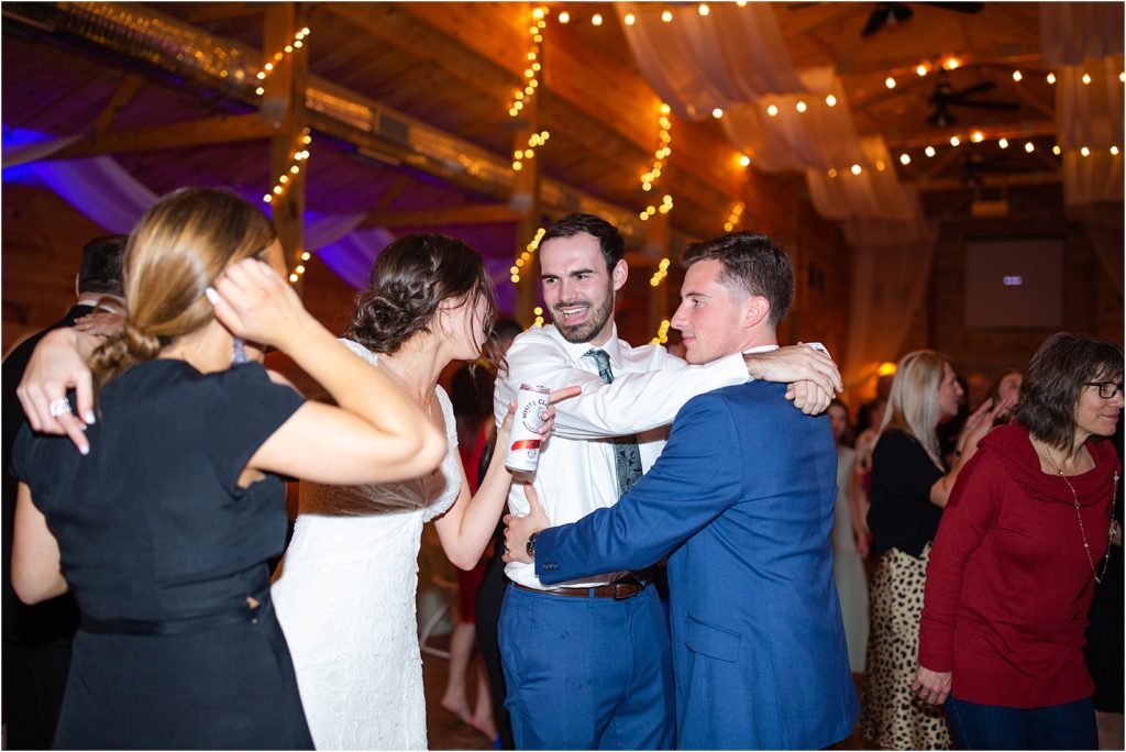 Groom dancing with friend while bride holds drink