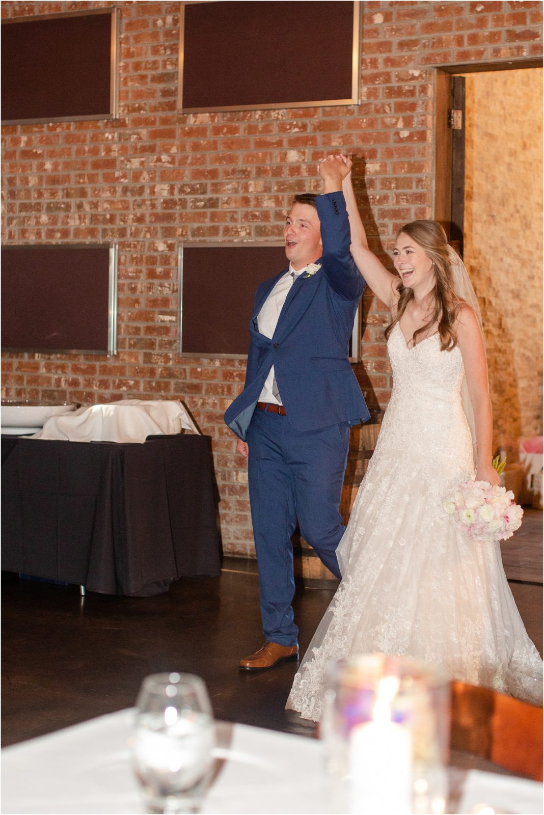 husband and wife holding up hands walking into reception