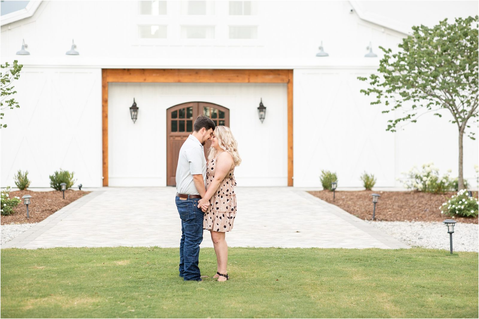 young couple embracing in front of white barn