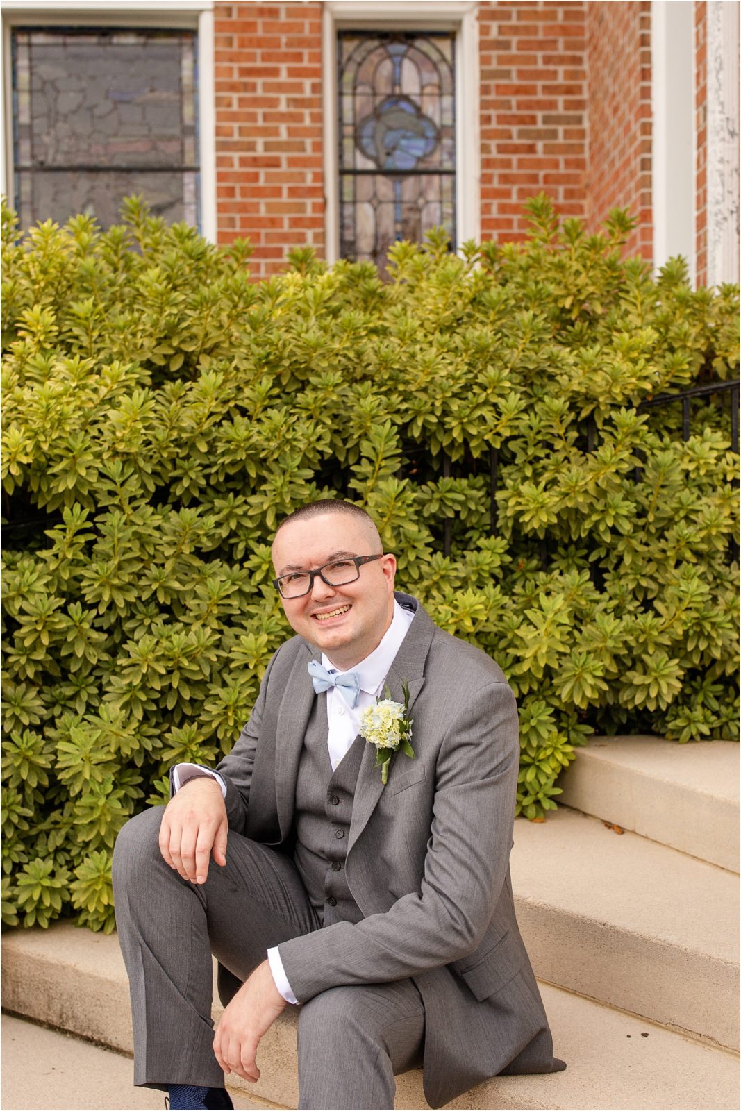Groom in grey suit sits on church steps
