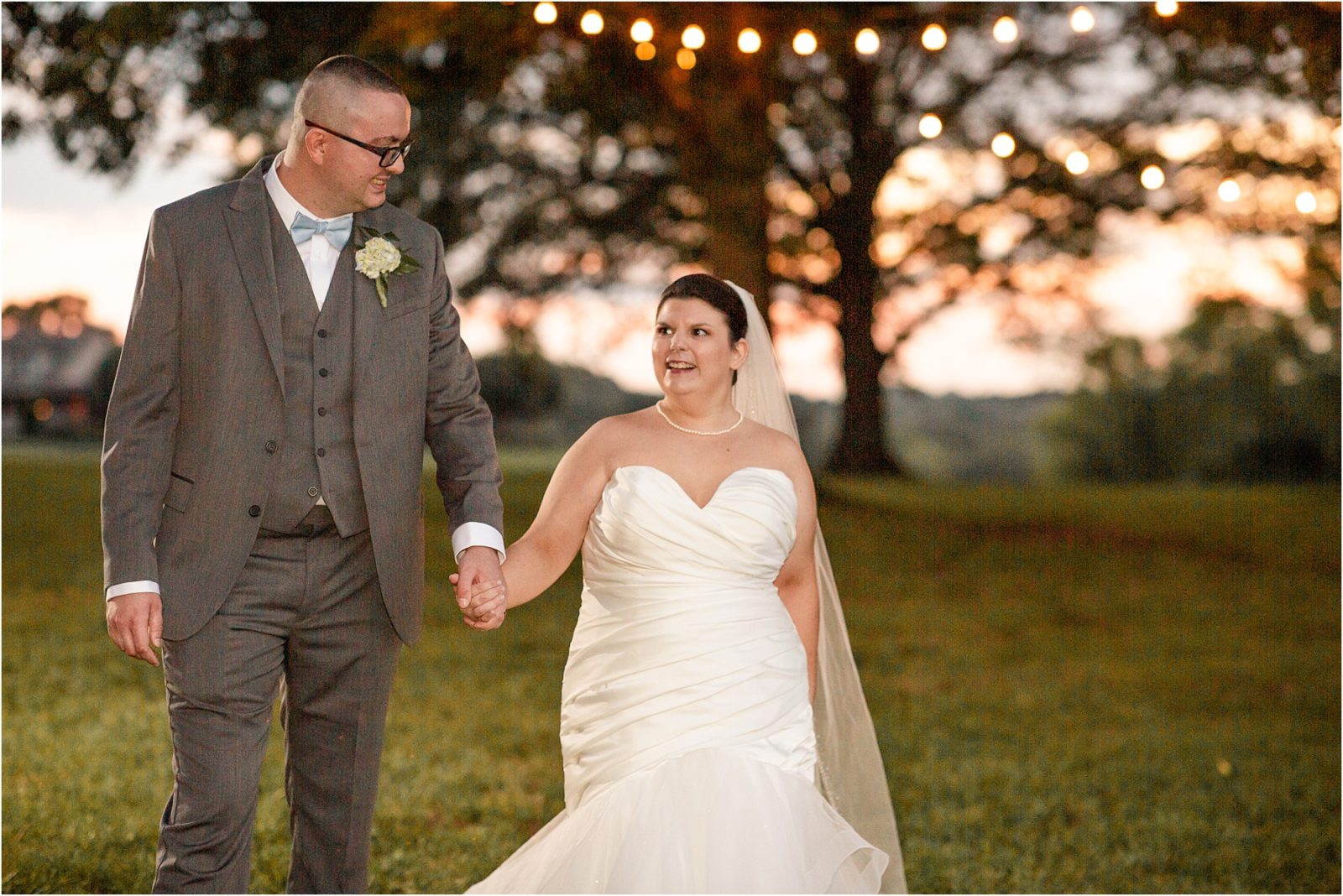 Just married couple walking under trees with string lights at barn wedding venue