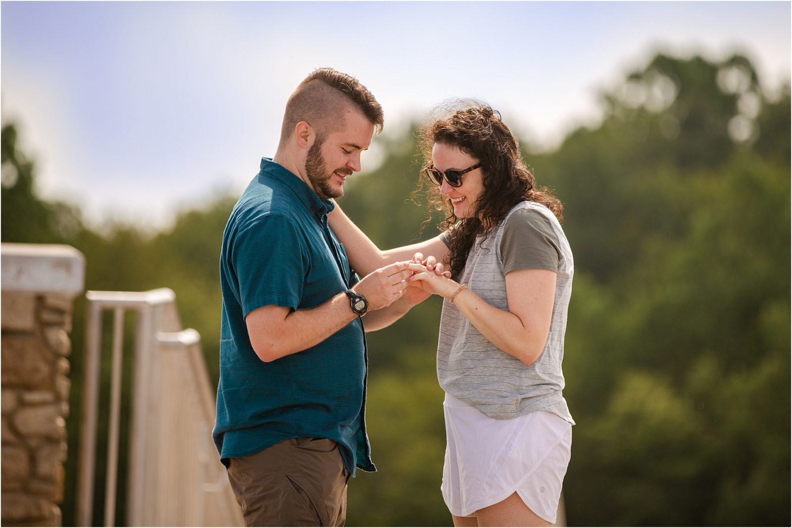 Woman with sunglasses looks at engagement ring as man puts it on her hand