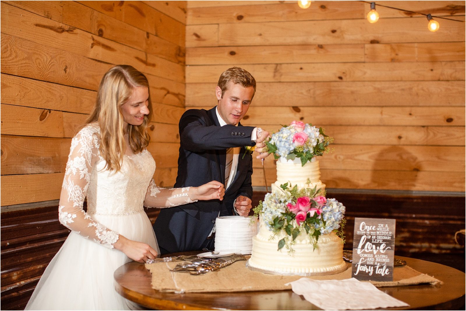 Groom cutting cake for bride in barn venue