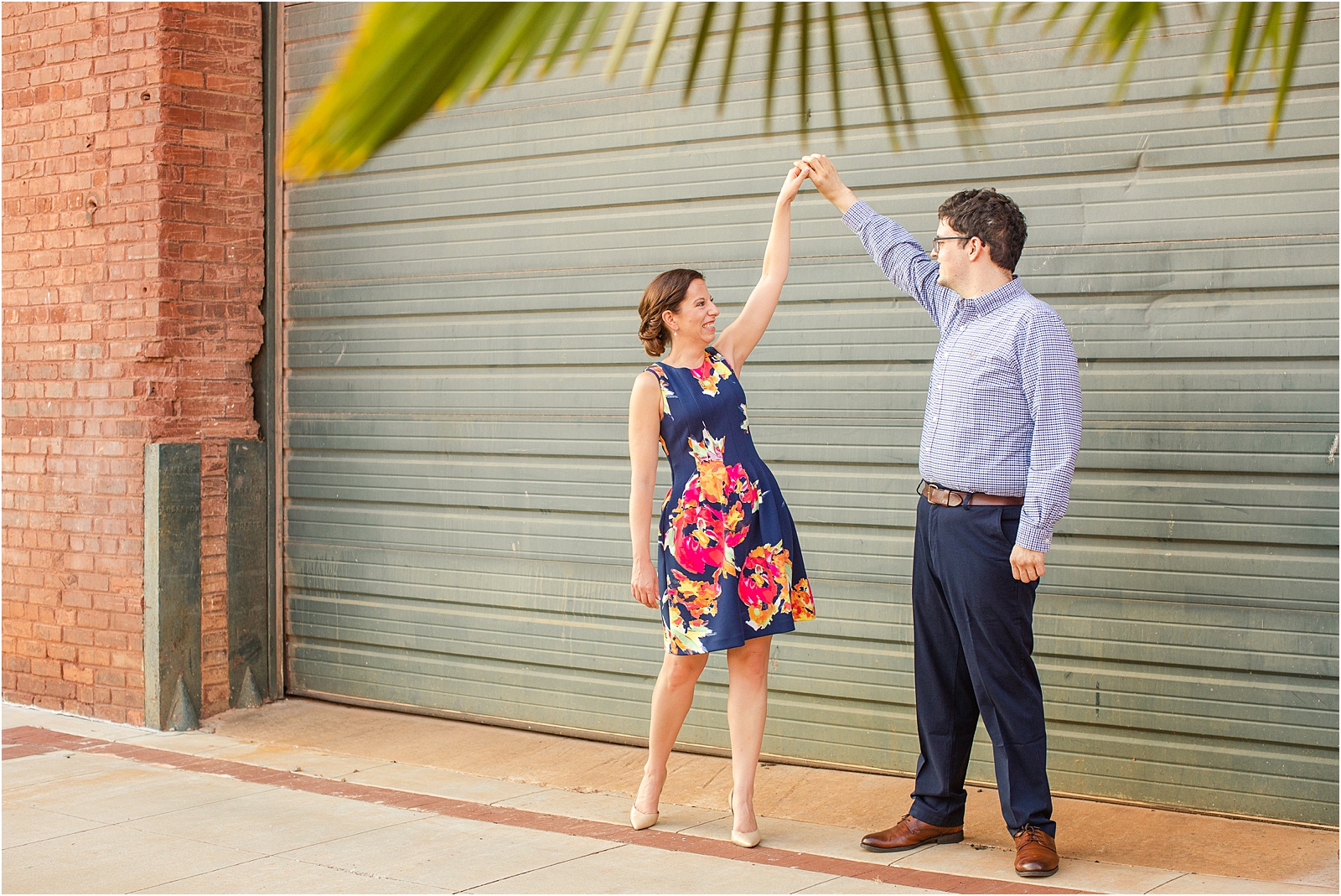 Happy engaged couple dancing next to brick building