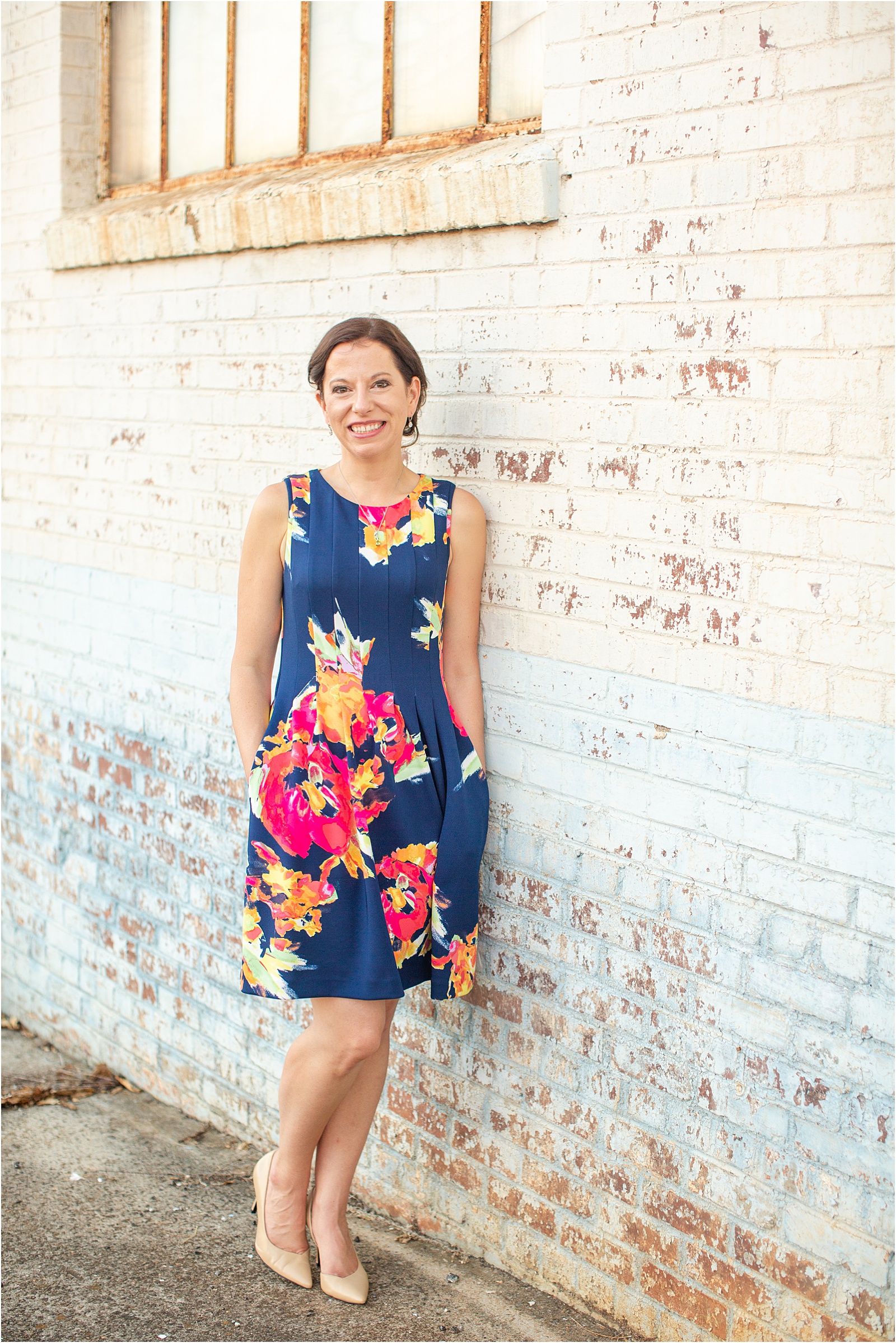 woman in flower dress leaning against brick wall in Anderson SC
