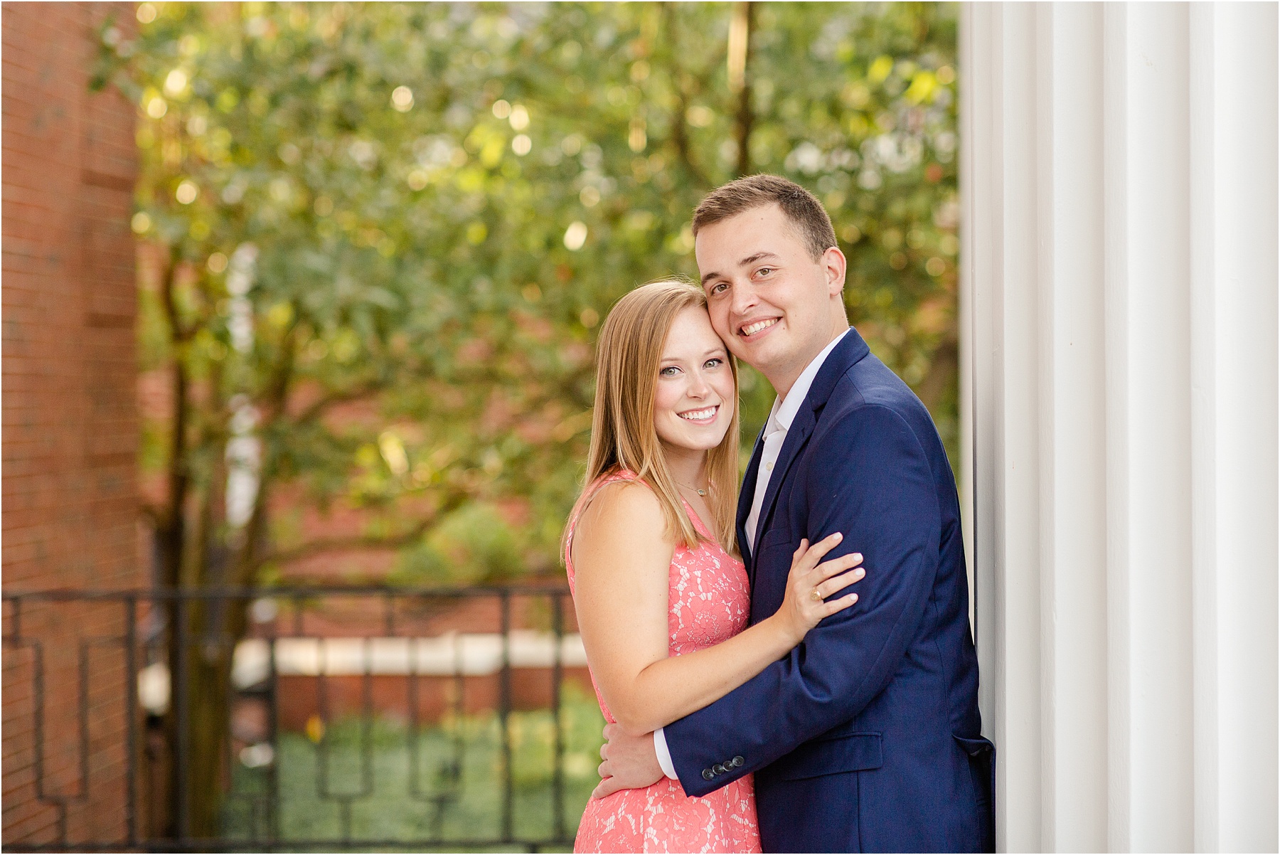 Engaged couple posing against white pillar