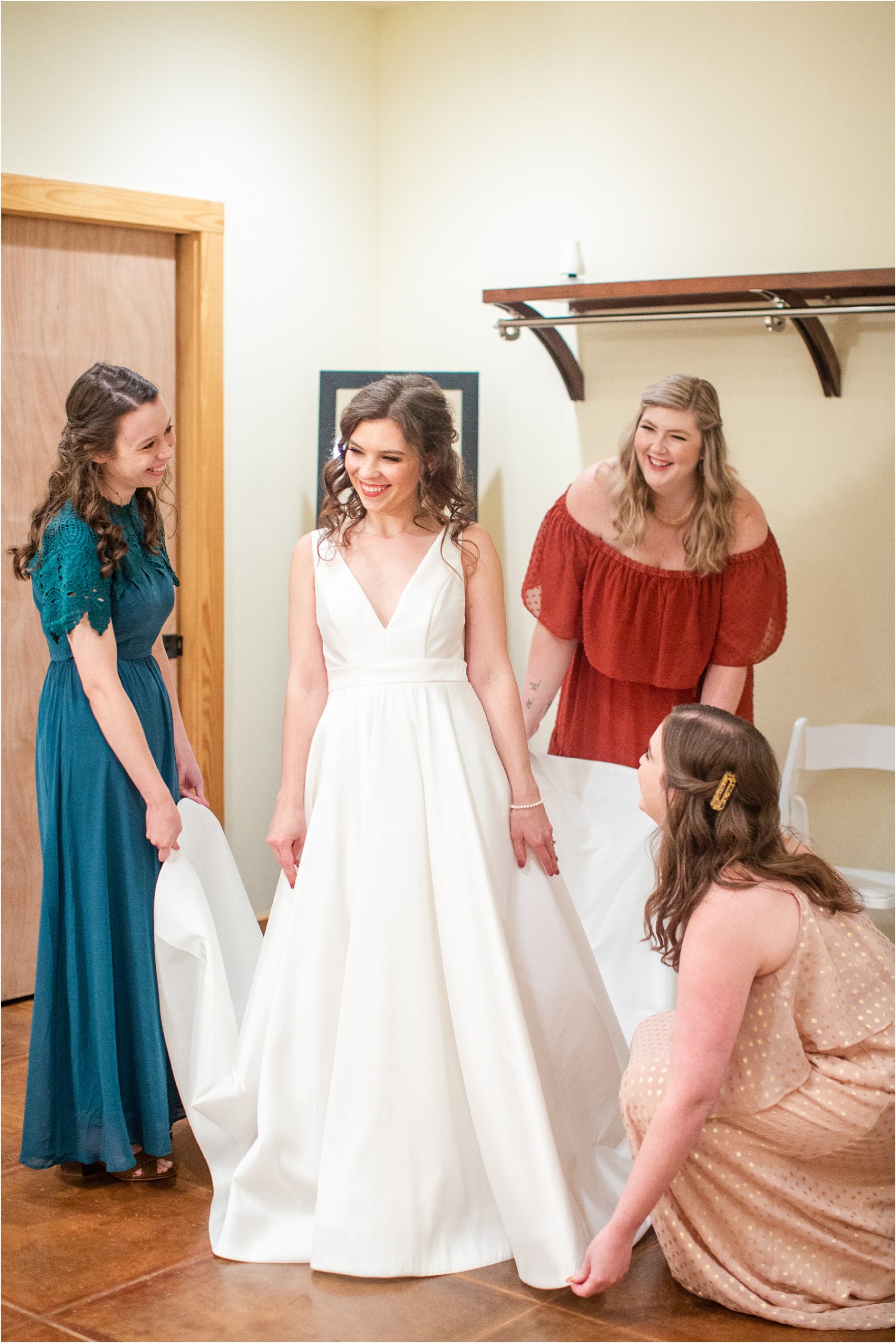 Three women hold wedding dress of bride