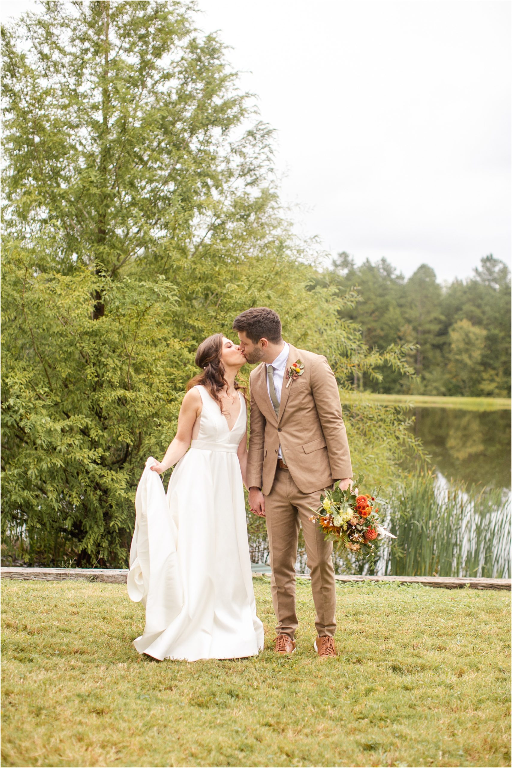 Newlywed couple kissing in front of vineyard pond