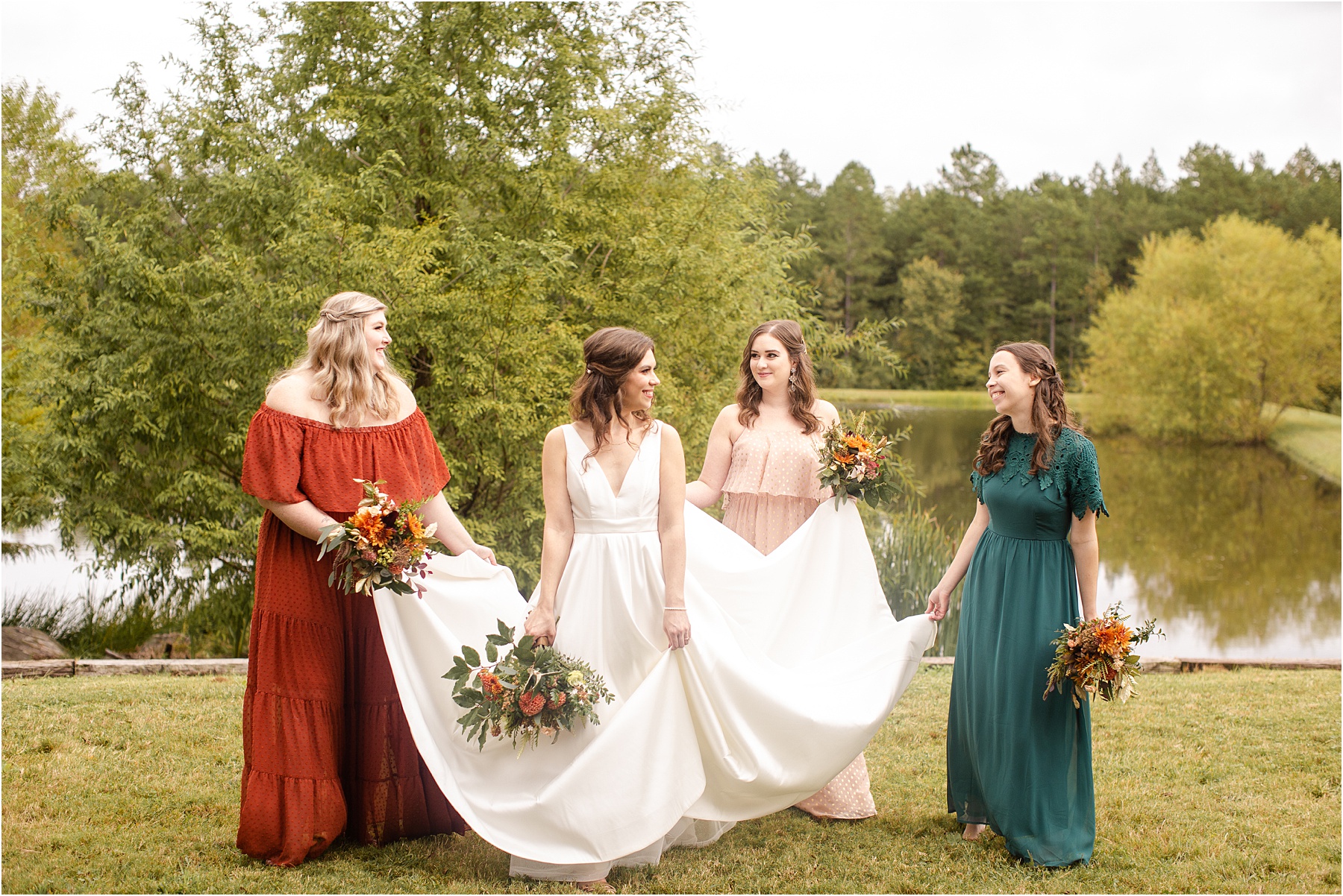Bridesmaids in colored dressed hold bride's wedding dress in the grass