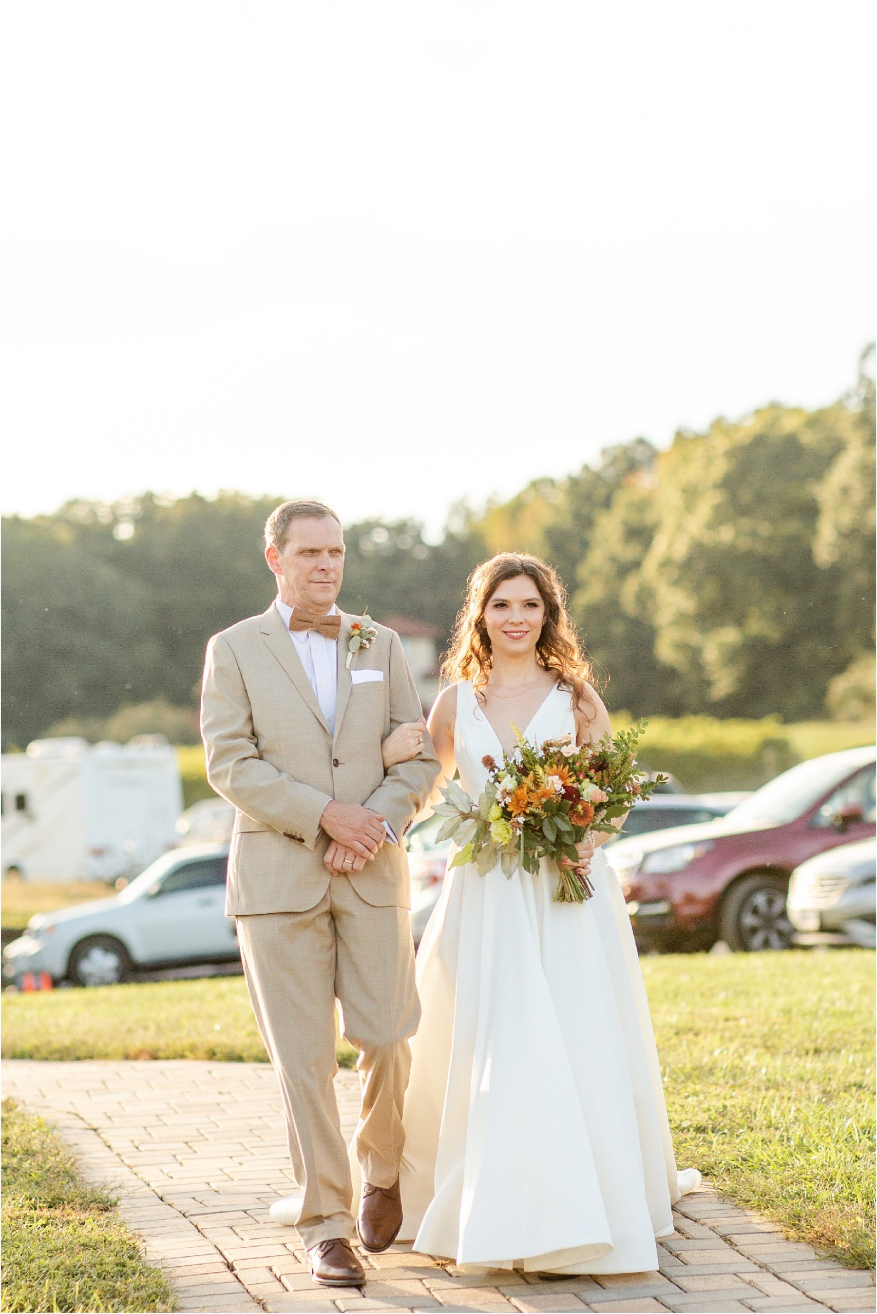 Man in tan suit walks with daughter in wedding dress holding flowers