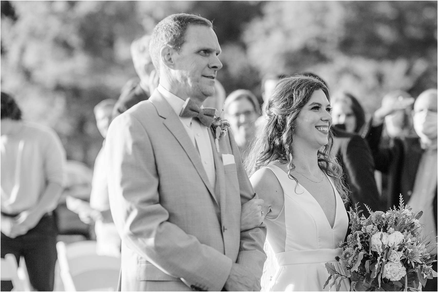 Woman in wedding dress smiles as she walks down the aisle with her dad