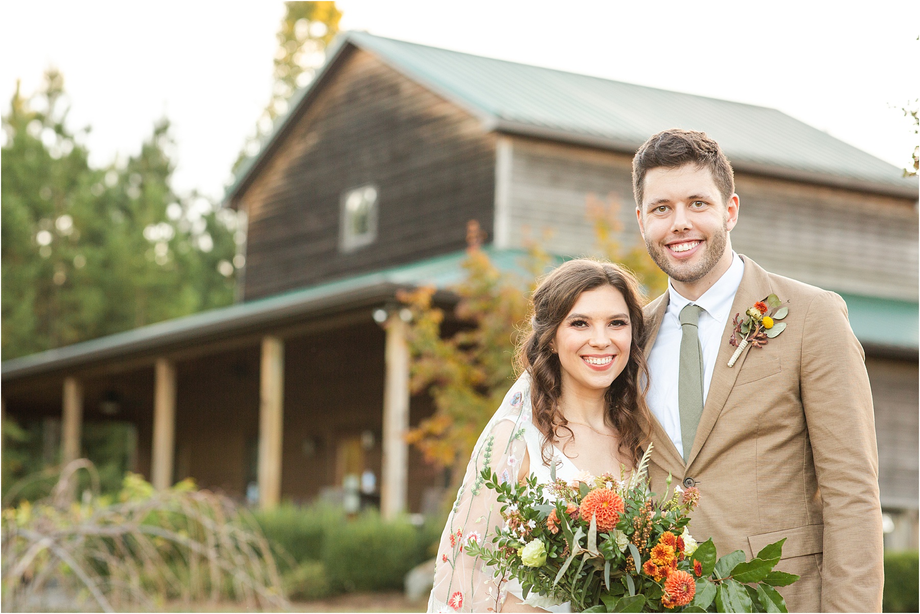 Groom with bride stands in front of old brown barn wedding venue