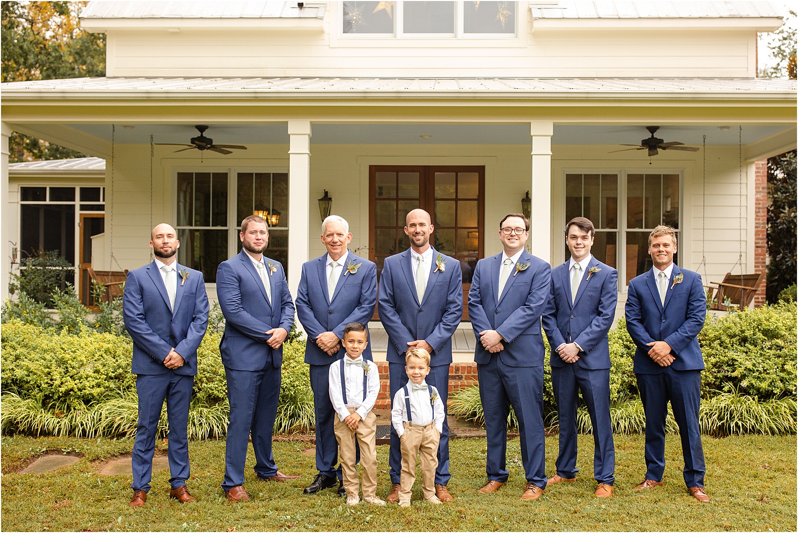 Line of men in dark blue suits pose in front of a house
