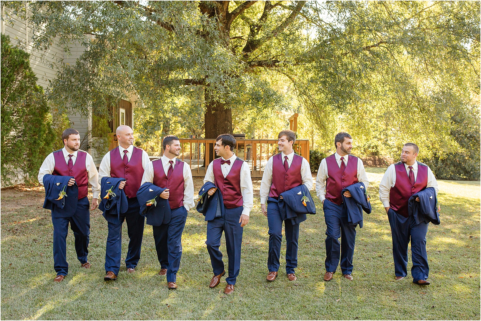 Group of groom and groomsmen with jackets over arms walking towards camera