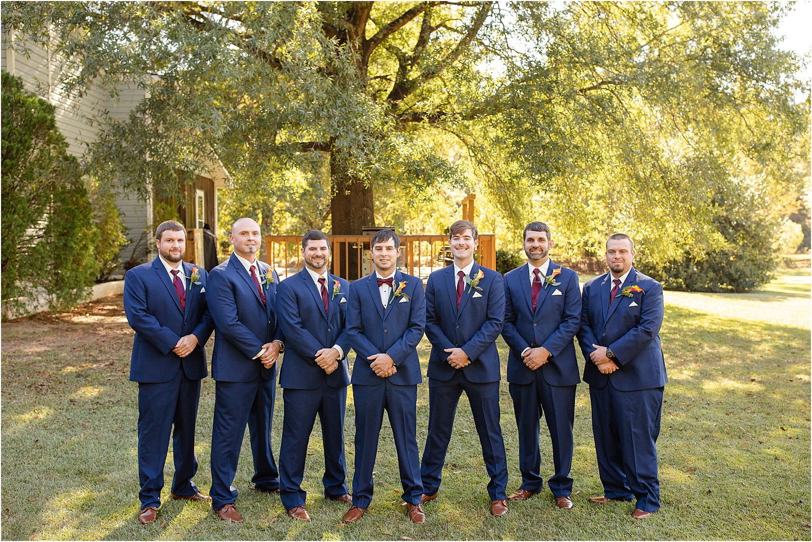 Groom with friends in navy suits and red time outside for pictures