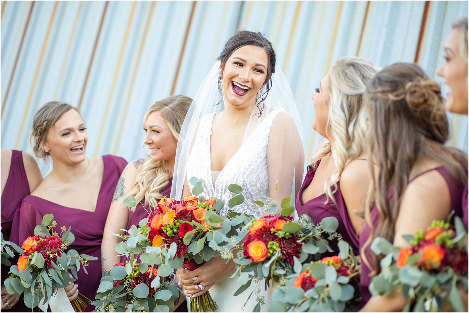bride laughs at her bridesmaids while all hold flowers