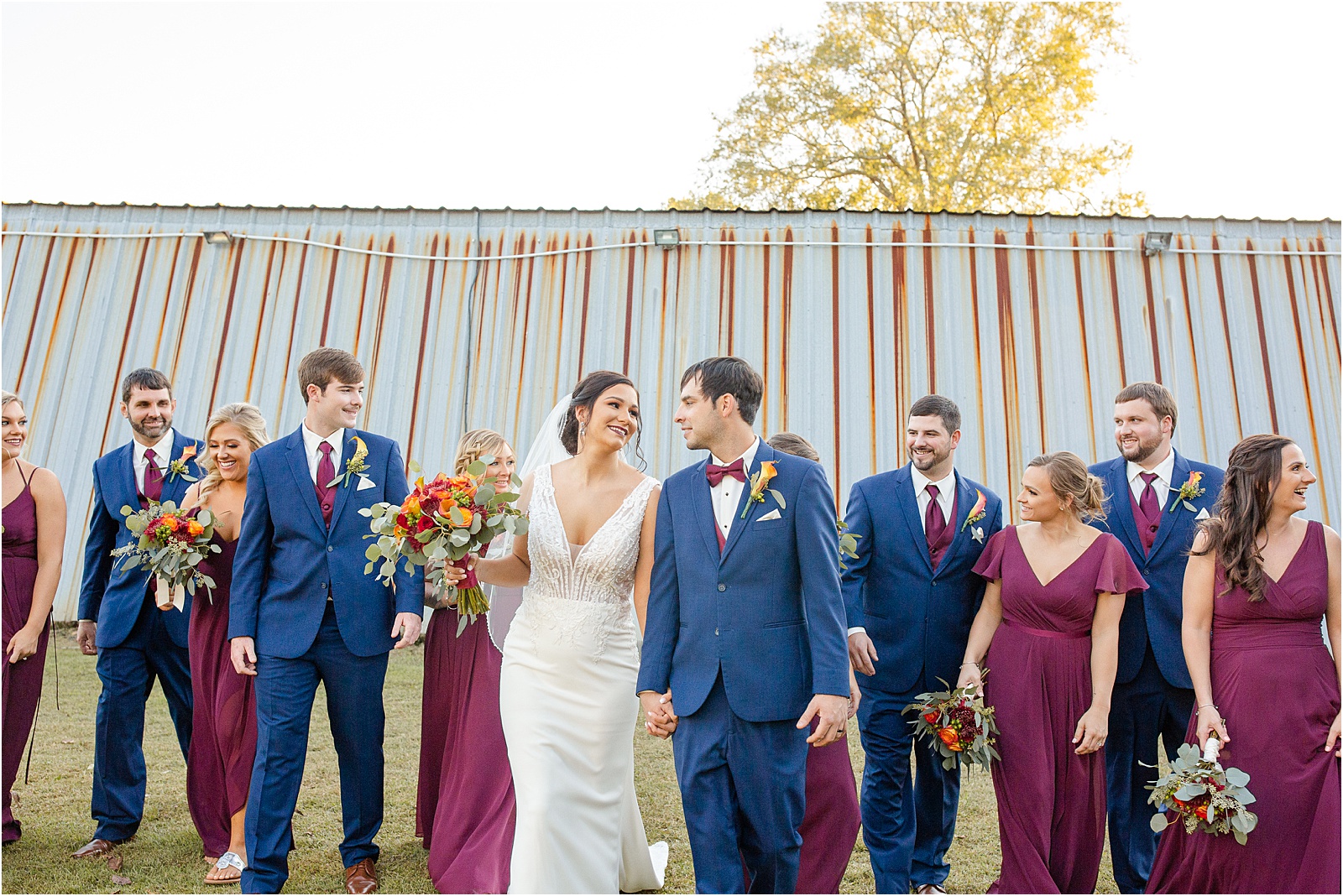 full bridal party walking towards camera with barn wedding venue in background