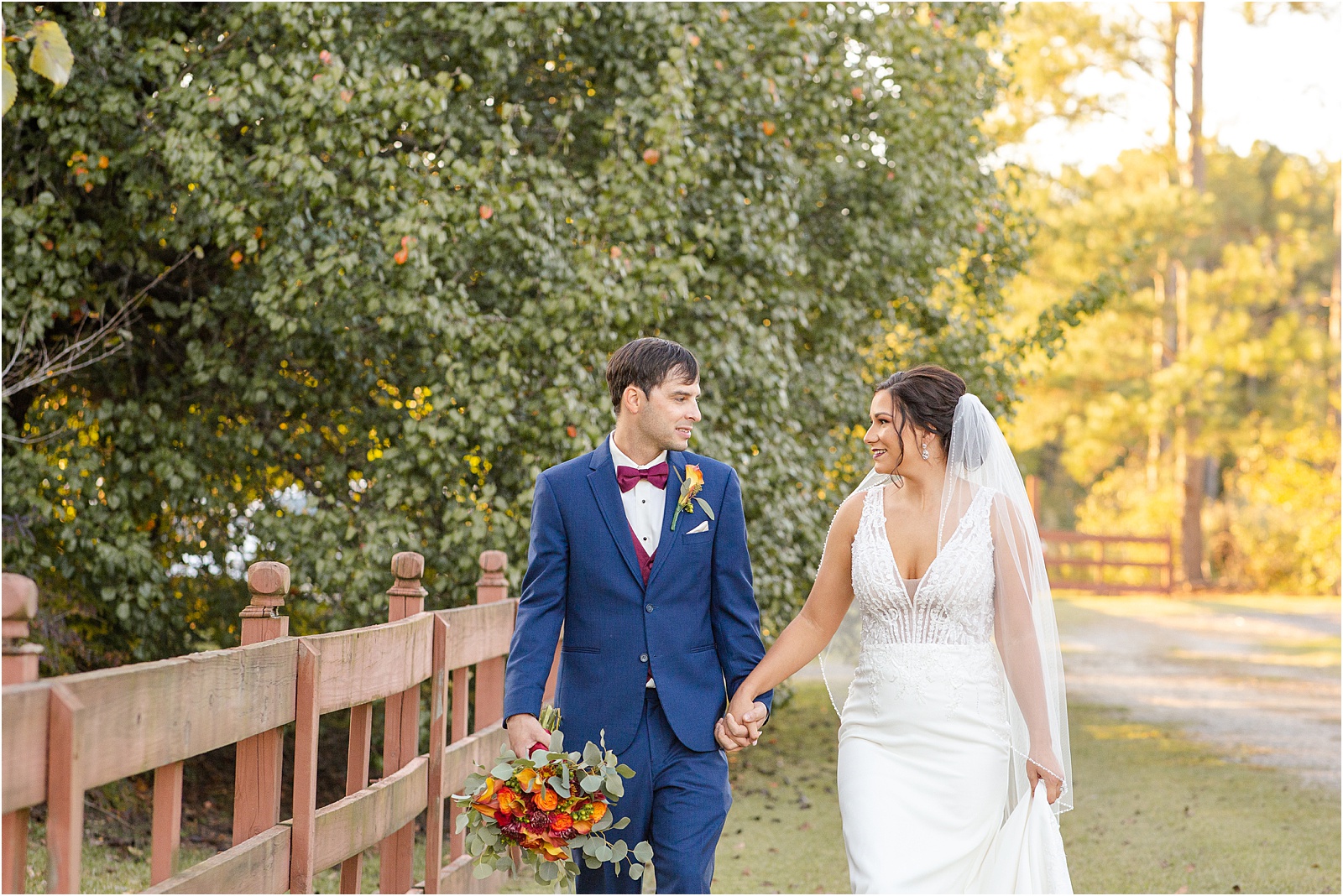 groom looks at bride as they walk along barn fence