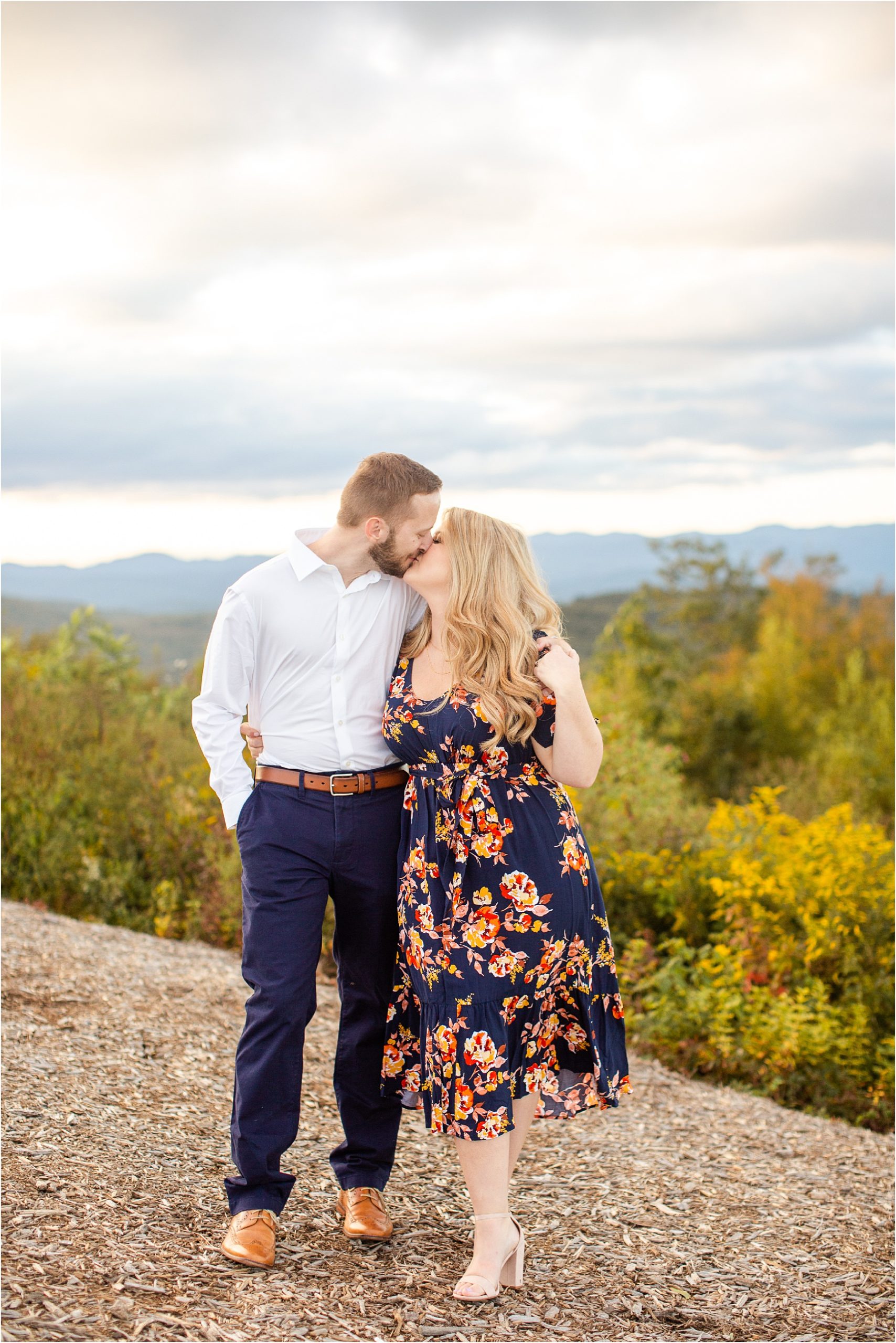 Engaged couple kissing on top of mountain