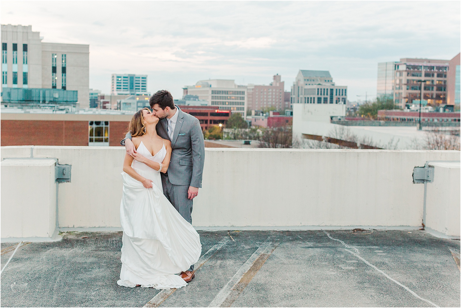 Groom has arm around bride kissing with greenville city in background