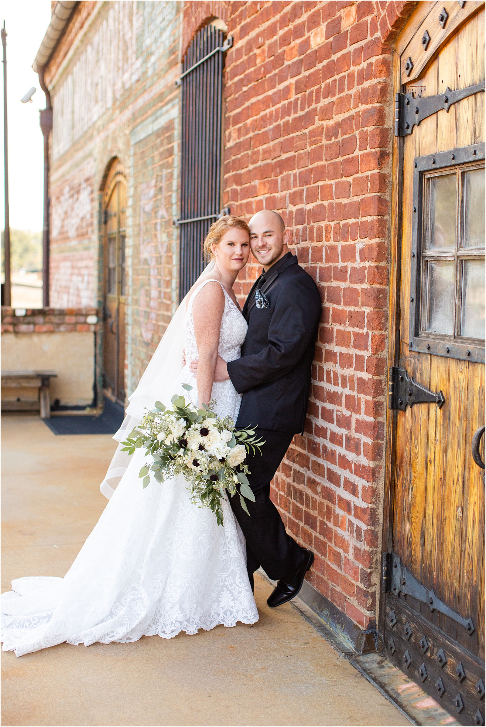 groom leaning against brick wall of old cigar warehouse with his bride