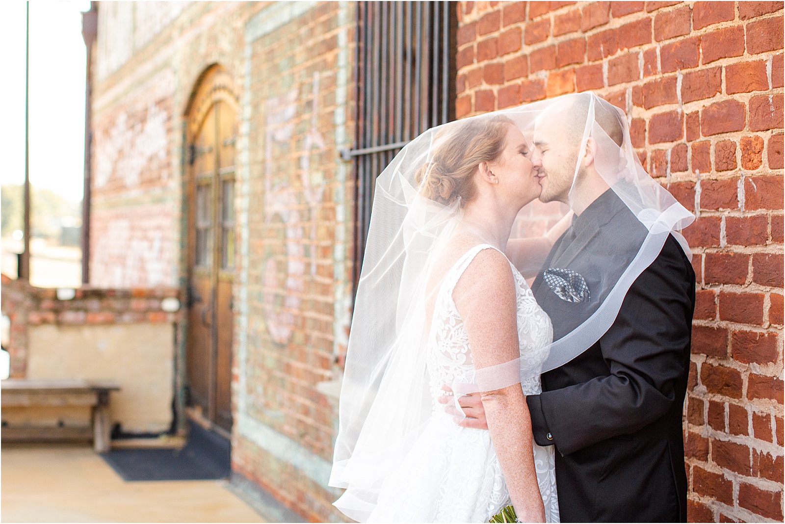 veil draped over newlyweds as they kiss