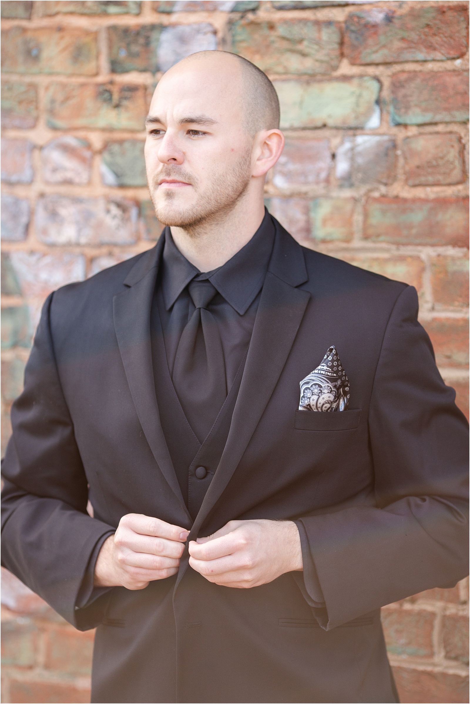 Groom looks off in distance as he buttons top button of jacket