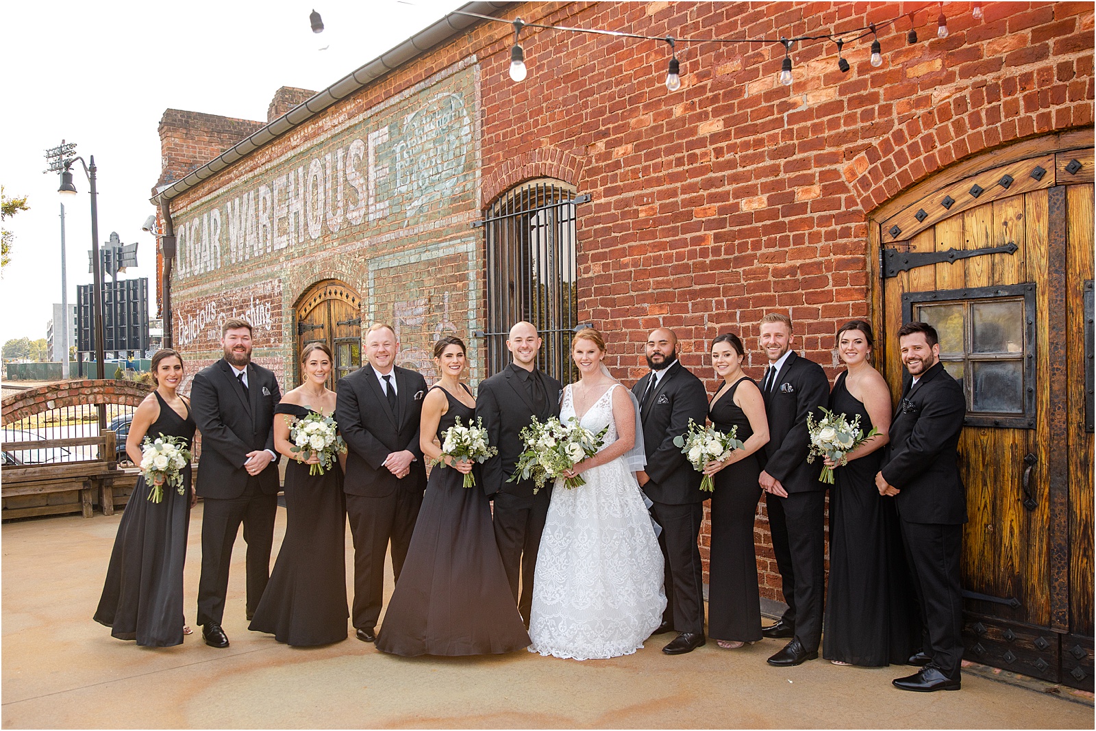 full bridal party in black suits pose with bride and groom