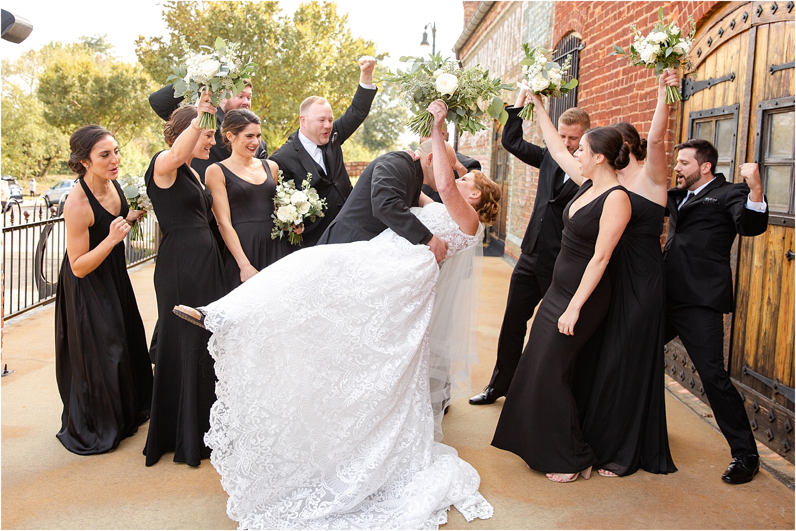 groom dips bride and kisses as bridal party celebrates