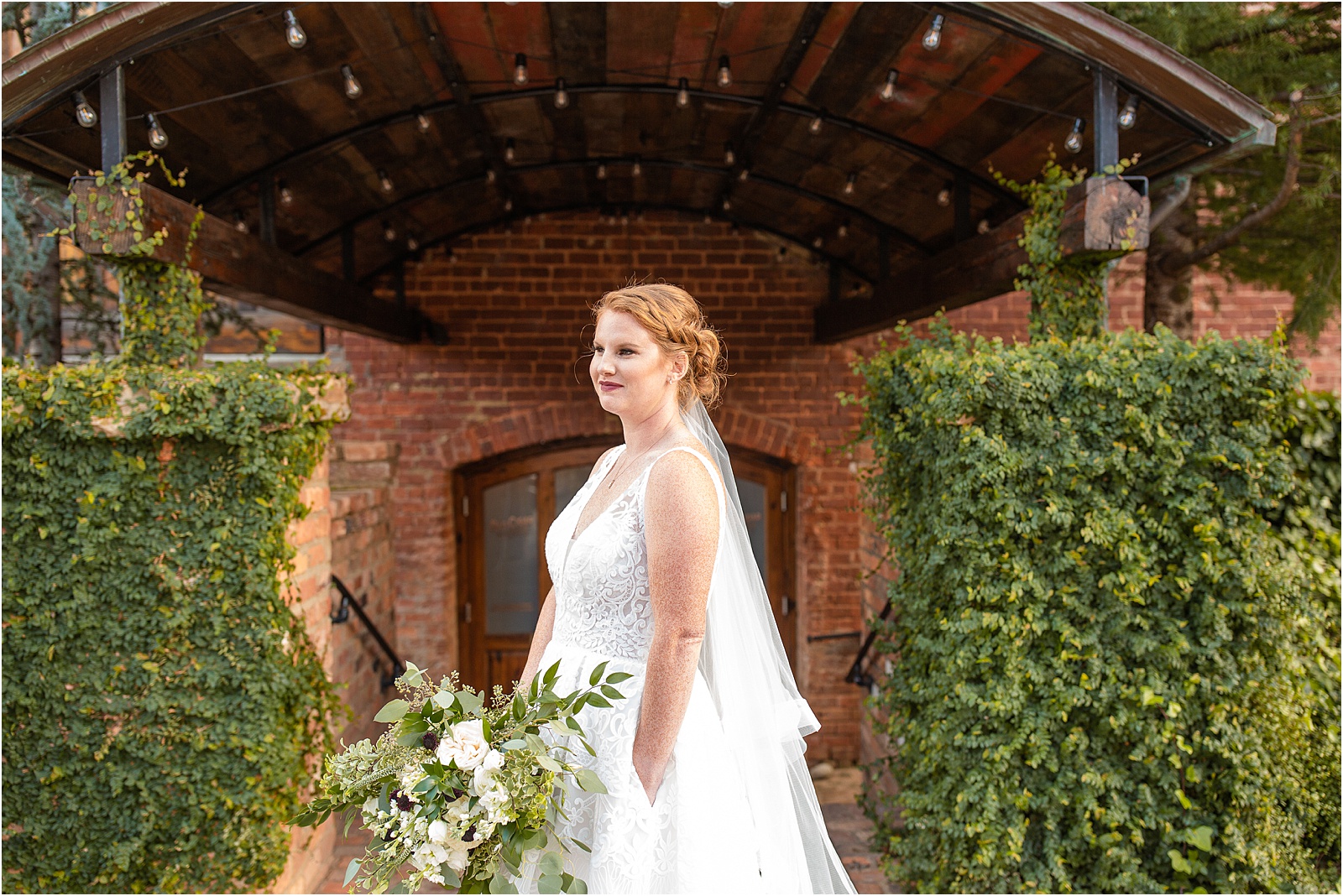 bride standing by herself next to brick building covered in ivy