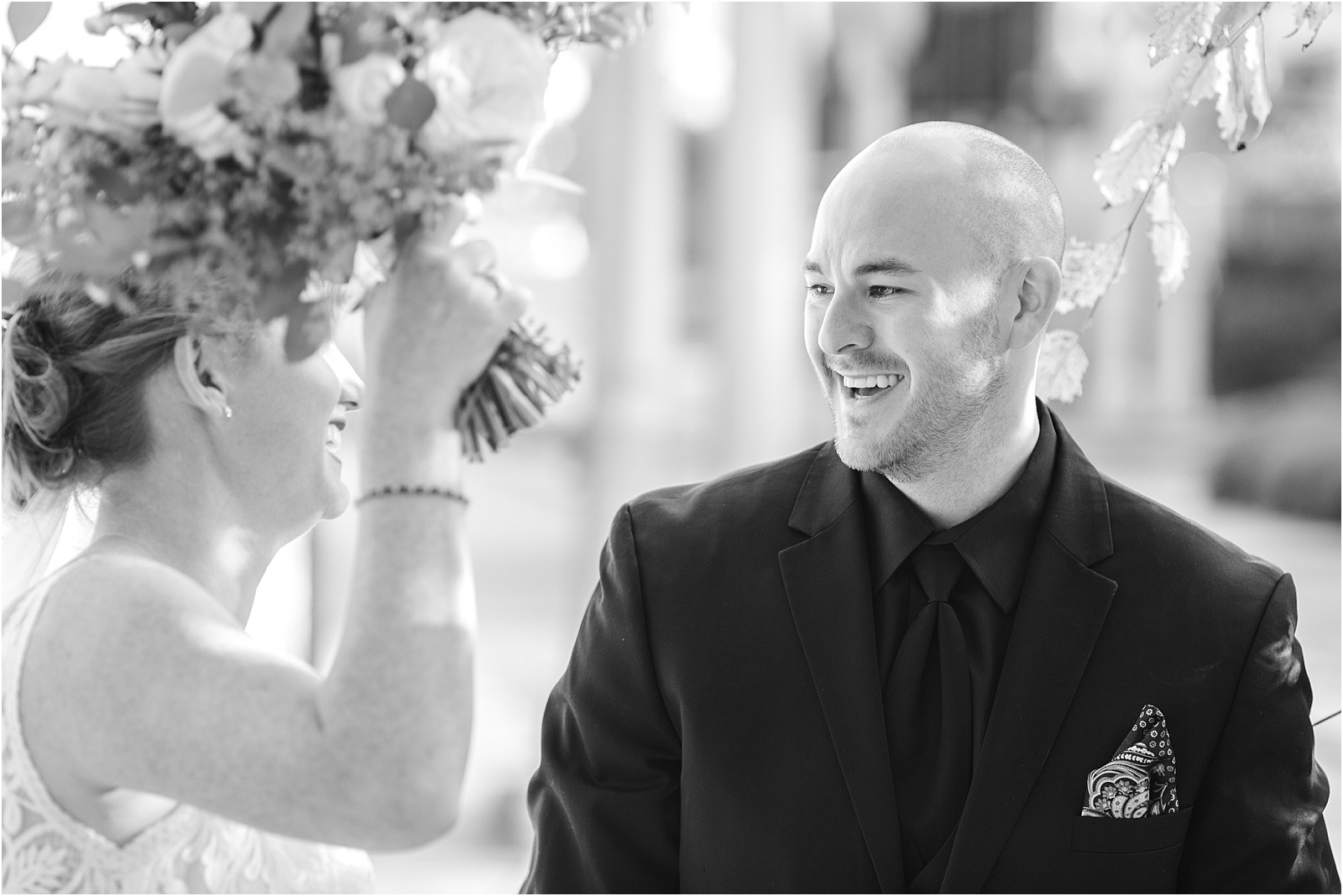 Groom in black suit laughs at his newlywed wife