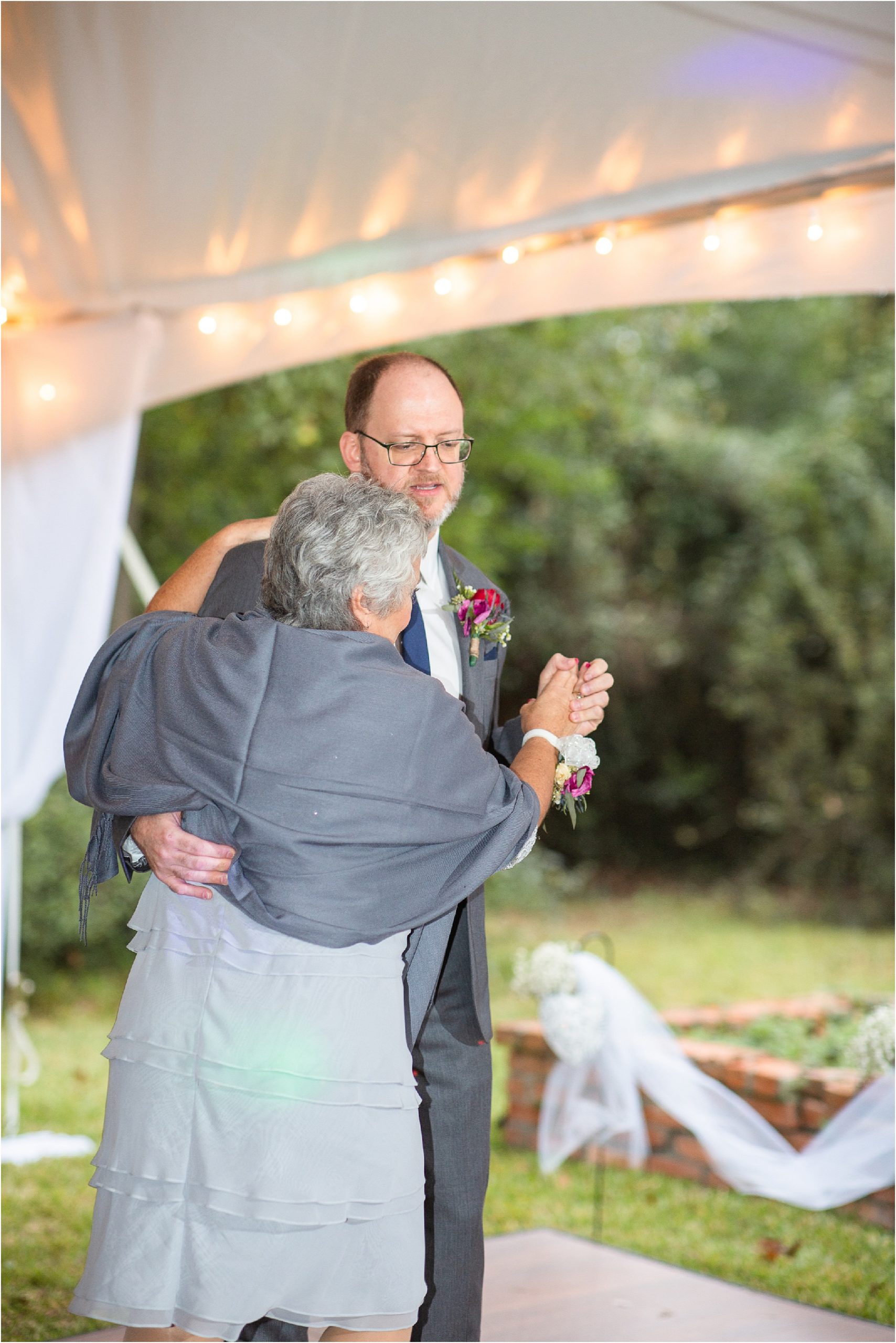 groom dances with mom under a white tent