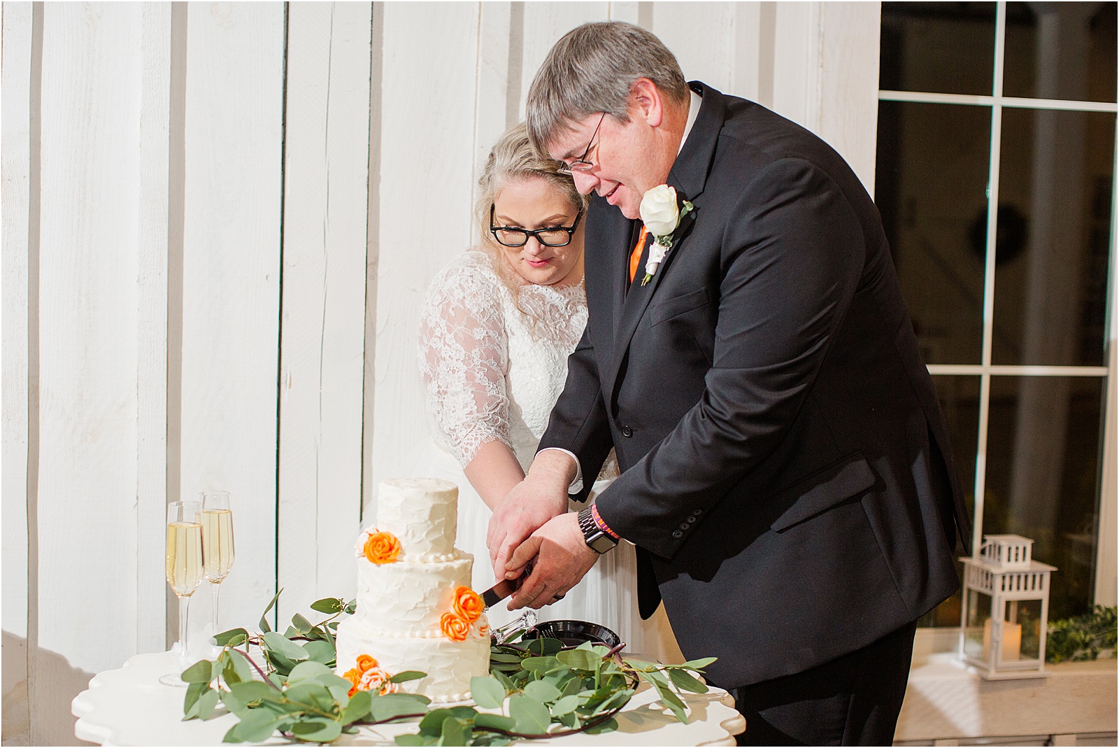 Newlyweds cutting wedding cake with orange flowers