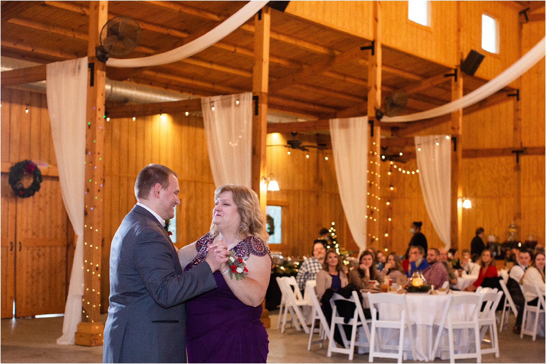 mom and groom dance in a barn venue with guests in background