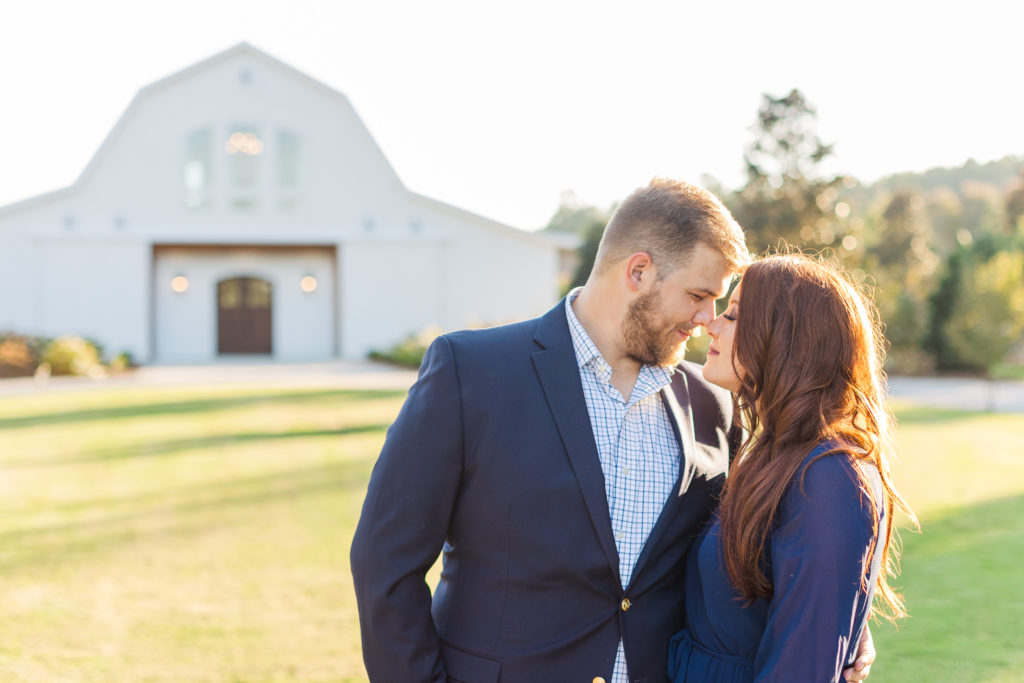 couple touching foreheads in front of white barn