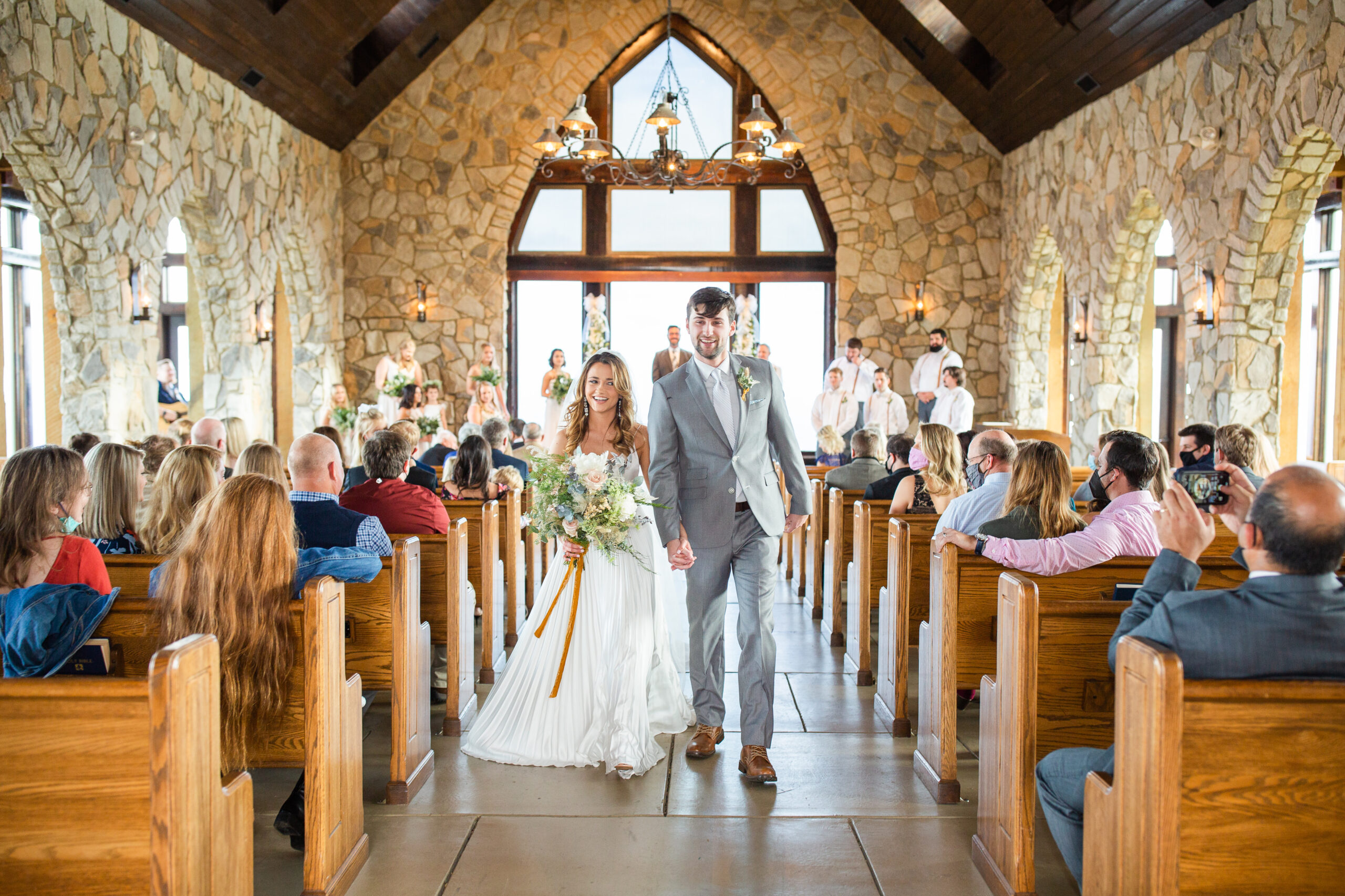 married couple walking down the aisle of glassy mountain chapel in